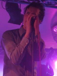 a man holding a microphone up to his face while standing in front of a purple light