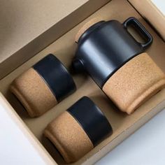 three black cups and two brown ones in a cardboard box on a white table top