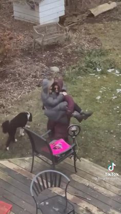 a woman sitting on a chair with a dog standing next to her in the yard