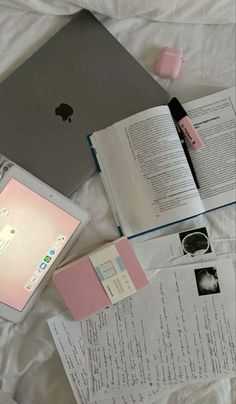 an open laptop computer sitting on top of a bed next to books and paper sheets