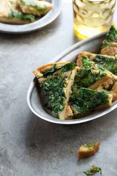 slices of spinach and cheese pizza on a plate next to a glass of wine