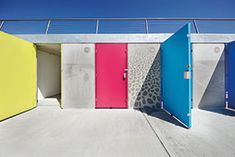 colorful doors are open in front of a white building with blue, yellow and pink walls