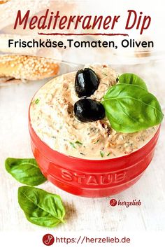 a red container filled with hummus and black olives next to baguettes