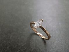 a gold ring with a pear shaped diamond in the center on a black table top