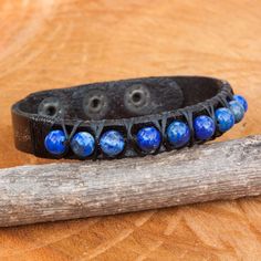 a black leather bracelet with blue glass beads on it and a wooden stick laying next to it