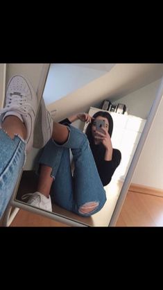 a woman taking a selfie with her cell phone while sitting on the floor in front of a mirror