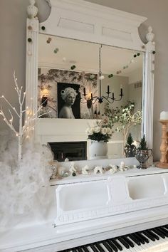 a white piano in front of a mirror with flowers and candles on the mantle next to it