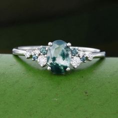 an oval cut blue and white diamond ring on top of a green surface with diamonds around it