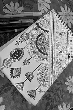 a notebook with an intricate design on it and two pens sitting next to each other