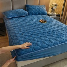 a person reaching for an unmade bed with blue sheets and pillows on the headboard