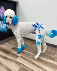 a white poodle with blue snowflakes on it's ears and tail