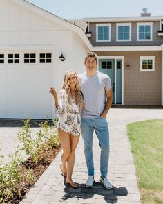 a young man and woman standing in front of a house with their arms around each other