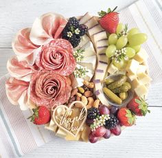 a platter filled with cheese, fruit and meats on a white wooden table