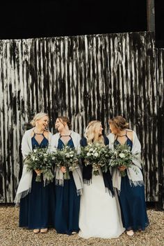 three bridesmaids laughing together in front of a barn wall with greenery and flowers