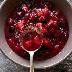 a white bowl filled with fruit on top of a table next to a silver spoon