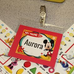 a name tag with mickey mouse on it is attached to a binder that says, my name is aurora