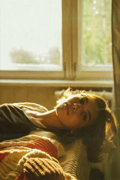 a woman laying on top of a bed next to a window