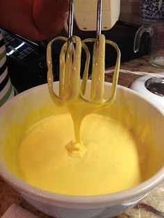 a mixing bowl filled with yellow liquid being whisked by two hand mixers