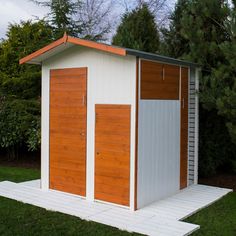 a white and brown shed sitting on top of a grass covered field next to trees