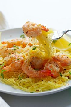 a white plate topped with pasta and shrimp next to lemon wedges on a table