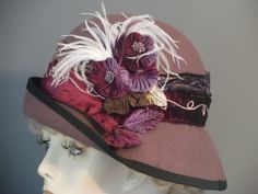 "This luscious mauve felt has been hand made using a vintage hat block. All hand made. Added flowers, feathers and 2 tone velvet band make this hat quite a statement piece. The 2.5\" band that encircles the crown is decorated with gold & lurex swirled trim, & sequins, against mauve and burgundy velvet. White small ostrich feathers, and light and dark purple flowers with wine, purple and green velvet leaves adorn the side in a lush melange. Black grosgrain ribbon trims the edge of brim. A special occasion hat for weddings, formal events, New Years, and any outdoor event. Fit 22.5\". I can adjust to fit other sizes." Handmade Formal Hats, Handmade Fitted Hats For Formal Occasions, Handmade Fitted Formal Hats, Handmade Elegant Wide Brim Hat Bands, Formal Fitted Handmade Hats, Elegant Handmade Felt Fedora Hat, Elegant Burgundy Hat For Winter, Elegant Handmade Adjustable Felt Hat, Fitted Burgundy Brimmed Hat