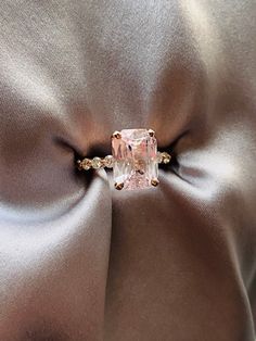 an engagement ring with a pink diamond in the center on a satin fabric back drop