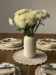 white flowers in a vase on a table with plates and napkins set around it