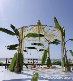 an outdoor wedding ceremony setup with hanging plants and chairs on the beach in front of the ocean