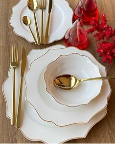 a table setting with gold utensils and red flowers on the side, along with white plates