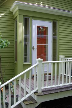 a small green house with a red door and white stairs leading up to the front door