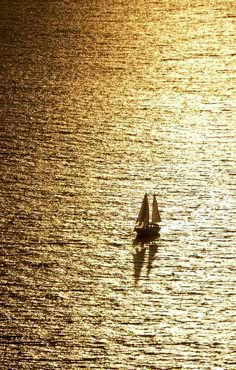 a small sailboat floating on top of a large body of water at sunset or sunrise