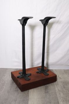 two black metal candlesticks sitting on top of a wooden stand in front of a white wall