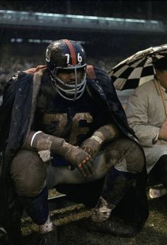 a football player sitting on the sidelines with an umbrella over his head while another man sits next to him