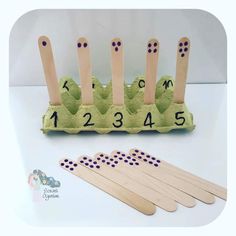 four wooden pegs with numbers on them next to an egg carton filled with eggs