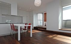 a dining room table with red chairs next to a white kitchen counter and window in the background