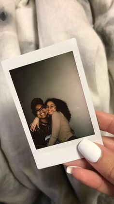 a woman holding up a polaroid photo with her arm around another woman's shoulder