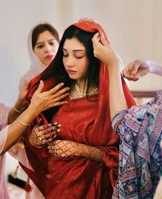 a woman getting her hair combed by another woman in a red sari and head scarf