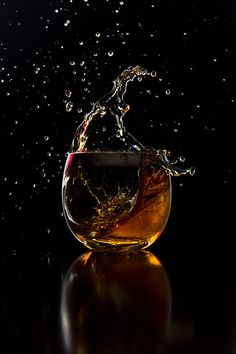 a wine glass filled with liquid on top of a table next to a black background