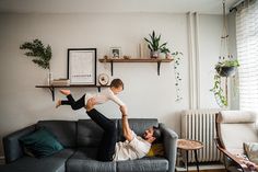 a man holding a child on his back while laying on top of a gray couch