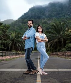 two people standing in the middle of an empty road with mountains in the background and palm trees on either side