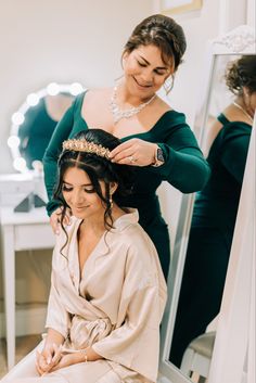 a woman sitting in front of a mirror while getting her hair combed by another woman