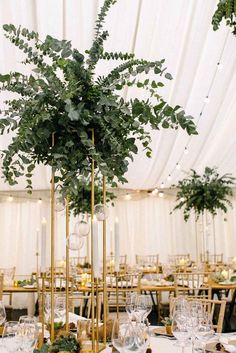 a tall gold vase filled with greenery on top of a white table cloth covered dining room