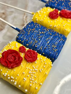 two cakes decorated with yellow and blue icing, red roses on sticks in the shape of flowers