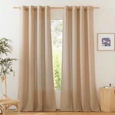 a living room with beige curtains and a wooden chair in front of a window that has a potted plant next to it