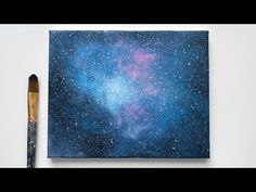 an acrylic paintbrush sitting next to a painting on a white surface with blue and pink stars