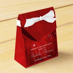 a red gift bag with a white bow on the front and bottom, sitting on a wooden surface