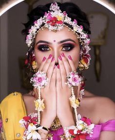 a woman with flowers in her hair covering her mouth and hands over her face while wearing an elaborate headdress