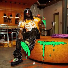 a man sitting on top of an orange ottoman covered in green paint and splatters