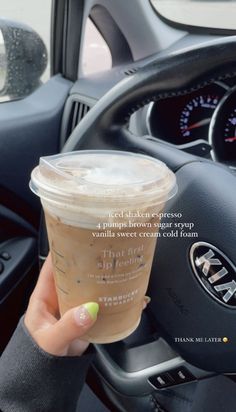 a woman holding up a cup of coffee in her car