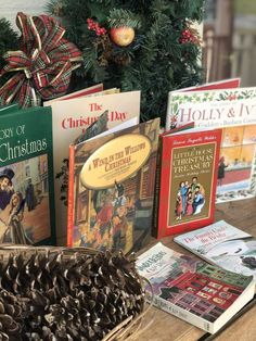 christmas books are sitting on a table next to a basket with pine cones in it